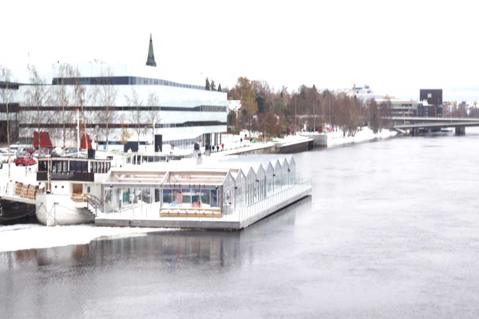 Snowy city scene with river, buildings, and floating structures.
