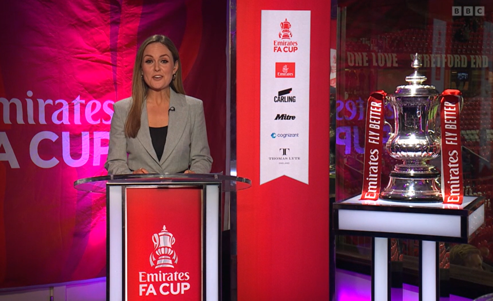 A woman stands at a podium presenting the Emirates FA Cup.