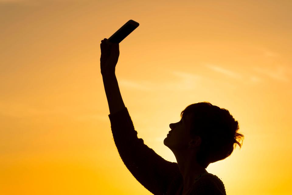 Silhouette of a person holding a cellphone up to the sky.