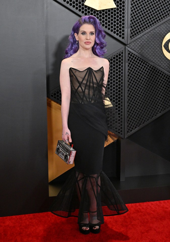 Kelly Osbourne at the Grammy Awards in a black sheer-paneled gown and purple hair, carrying a boombox-shaped purse.