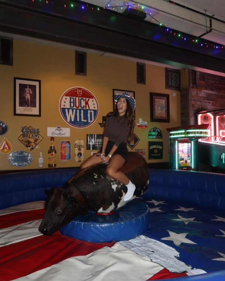 Woman riding a mechanical bull in a bar.