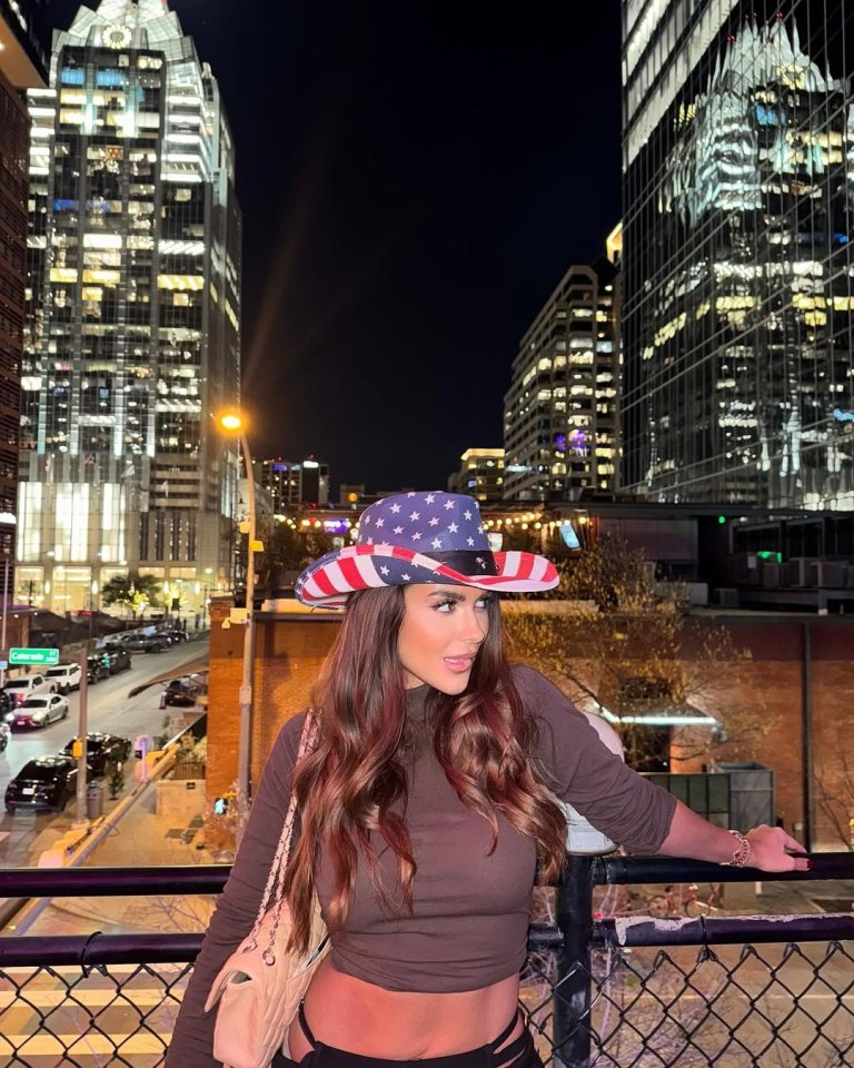 Woman in American flag cowboy hat on city rooftop.