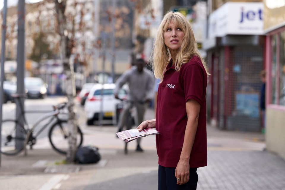 Woman in maroon shirt holding pamphlets on a city street.