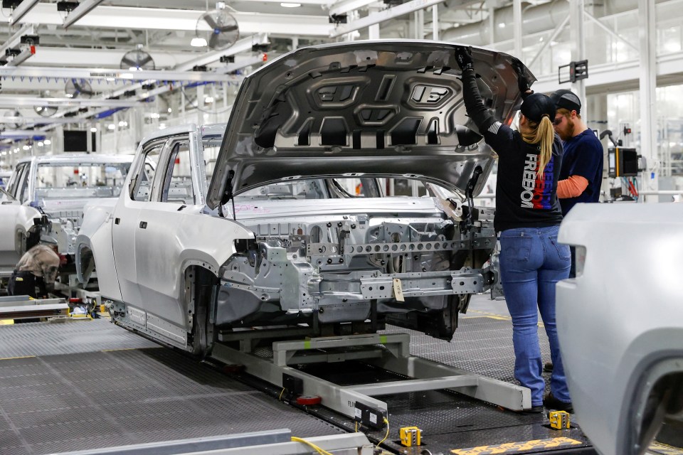 Workers assembling an electric vehicle on an assembly line.