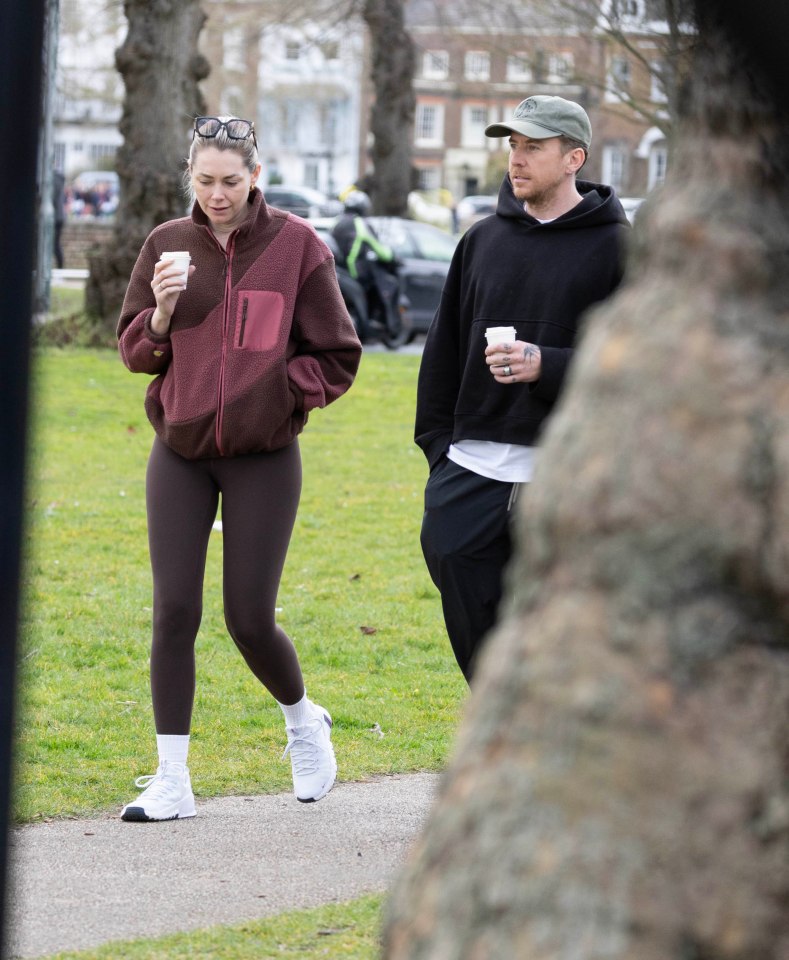 Danny and Georgia Jones walking in a park, holding coffees.