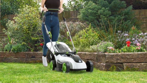 Person using a Gtech lawnmower on a grassy lawn.