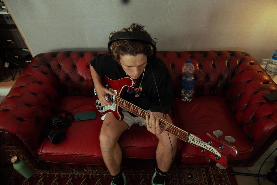 Person sitting on a red couch playing a bass guitar.