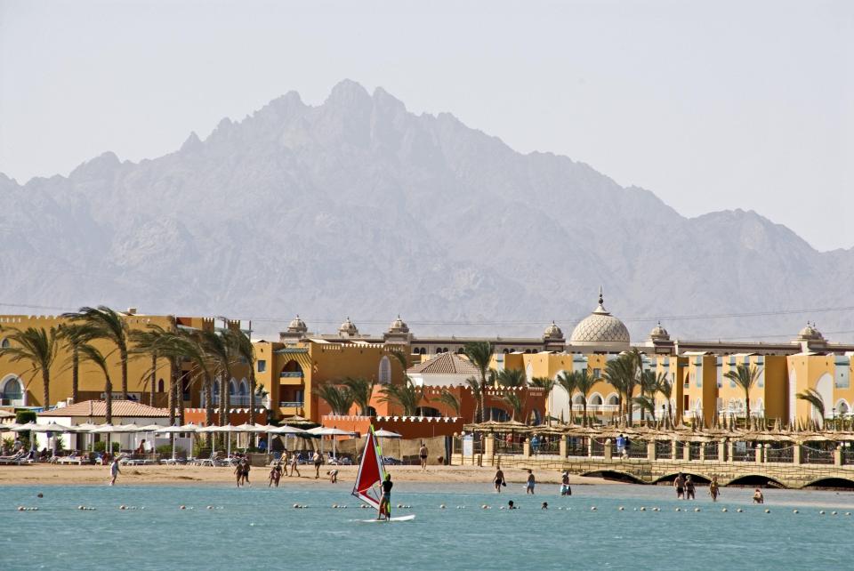 Windsurfer on a beach with a resort and mountains in the background.