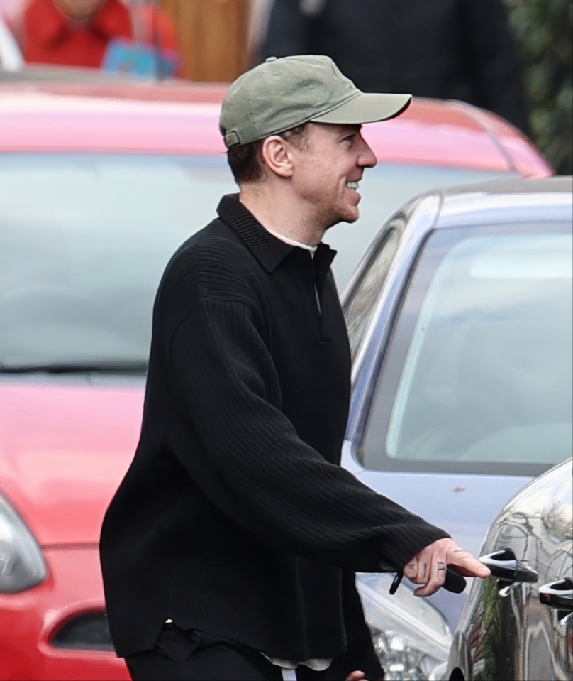 Danny Jones smiling while walking near cars.