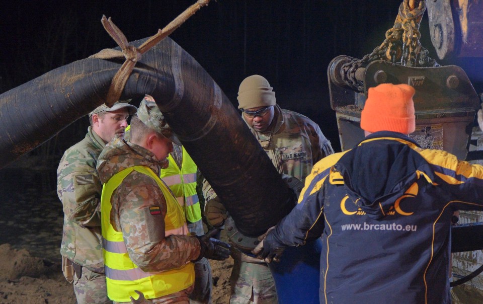 US and Lithuanian Army soldiers and emergency personnel assembling a water pump to recover a submerged vehicle.