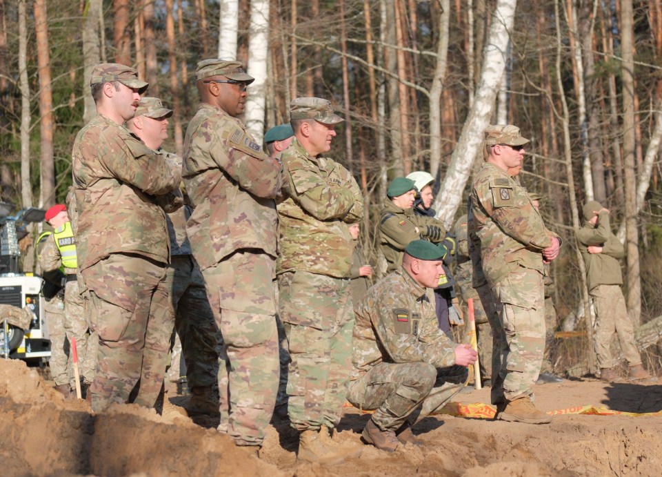 U.S., Lithuanian, and emergency services personnel observing recovery efforts for a submerged military vehicle.