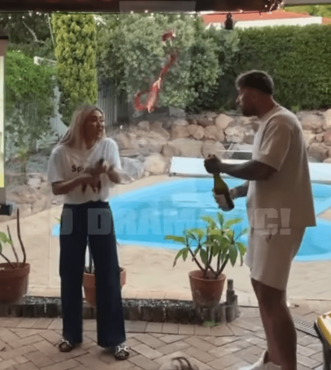 Couple opening champagne by a pool.