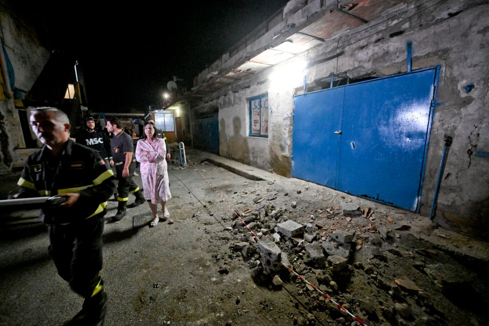 Emergency responders and a resident stand amidst rubble in a damaged building.