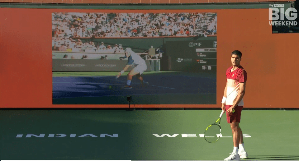 Tennis player on court with jumbotron showing tennis match.