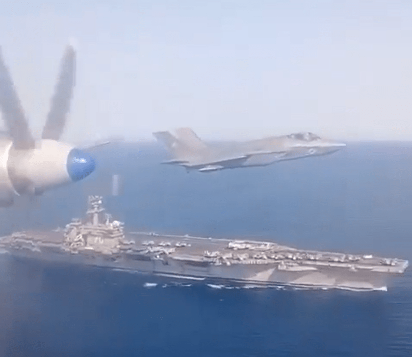 F-35 fighter jet flying over an aircraft carrier.