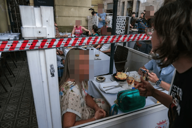 Patrons dining at an outdoor restaurant separated by plastic barriers.
