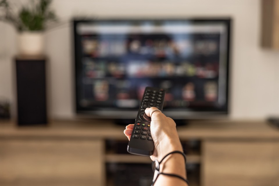 Woman's hand holding a smart TV remote, with a streaming service screen in the background.