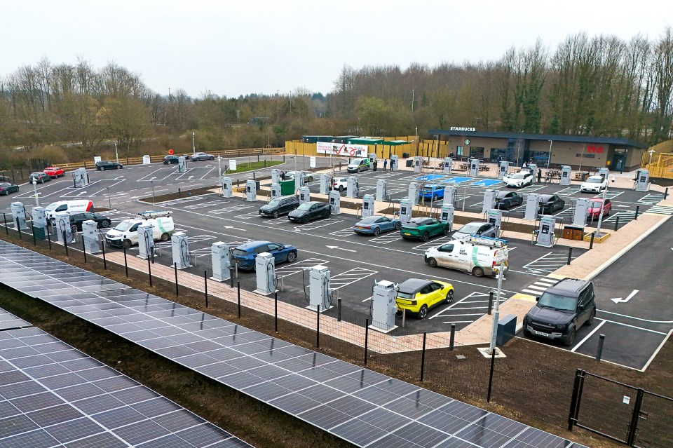 Aerial view of a large solar-powered electric vehicle charging station with numerous cars charging.