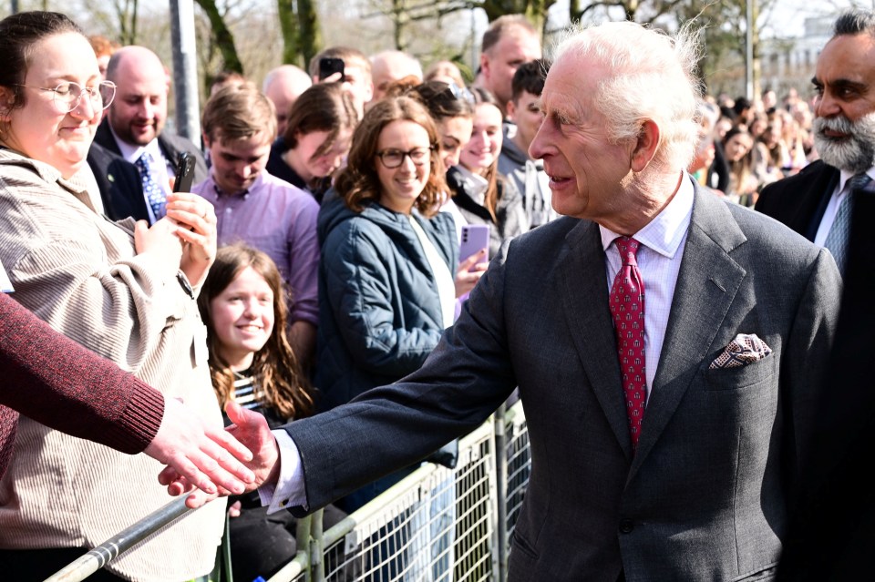 King Charles III shaking hands with well-wishers at a cancer research center.
