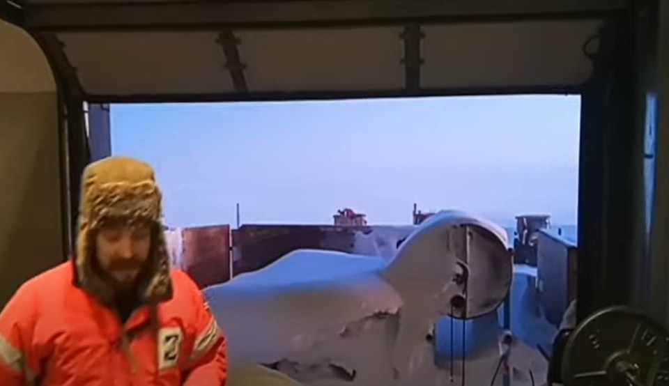 Antarctic adventurer in orange jacket looking out at snow-covered landscape.