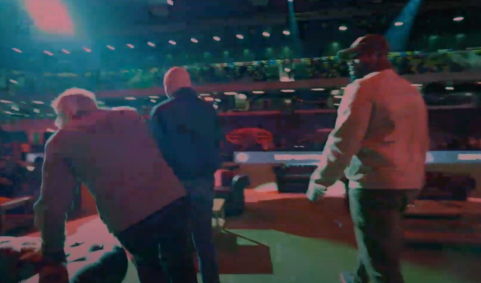Three people walking away from the camera in a large venue.