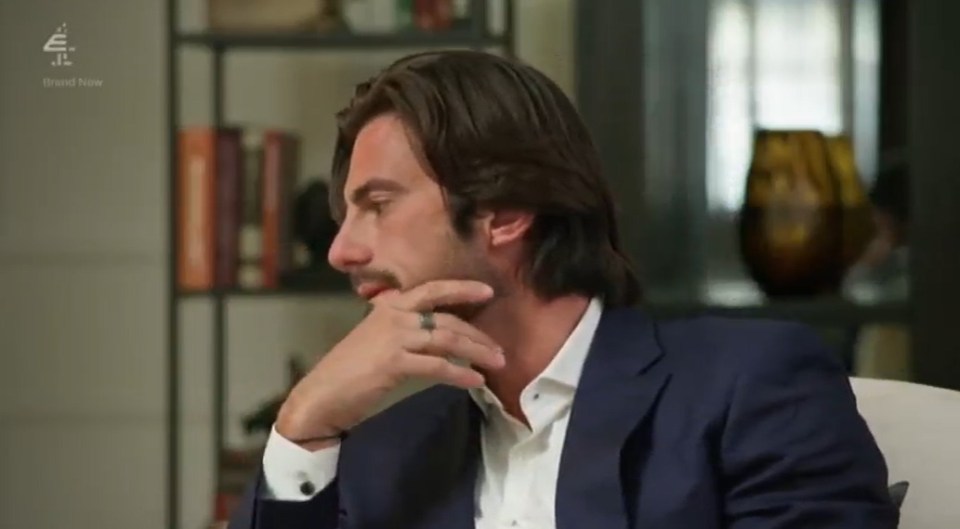 A man in a suit thoughtfully touches his chin.