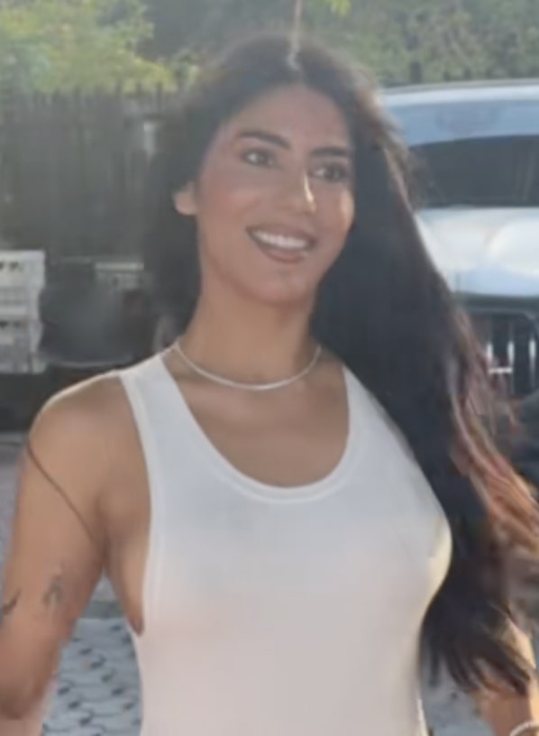A woman with long dark hair wearing a white tank top.