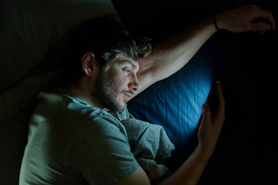 Man lying in bed using a smartphone at night.