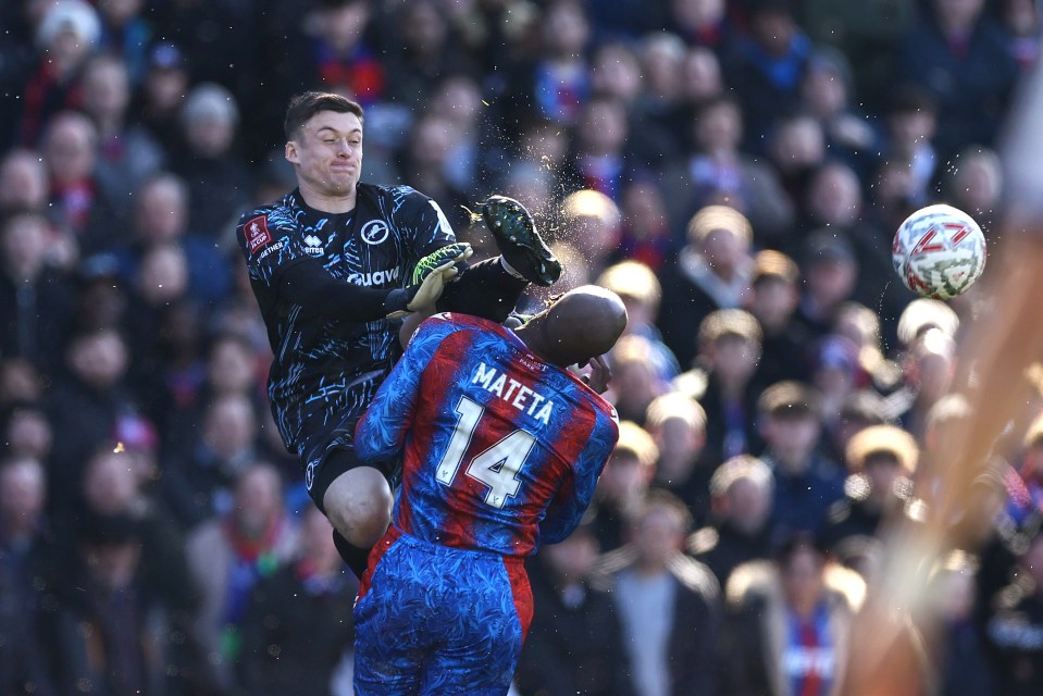 A soccer goalkeeper karate kicks an opposing player in the head during a match.