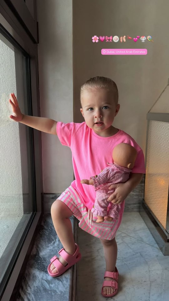 Toddler in pink holding a doll in Dubai.
