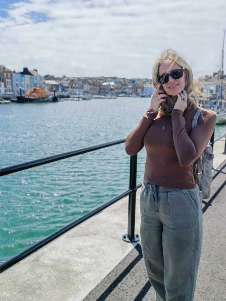 Woman standing by harbor wearing sunglasses and a backpack.