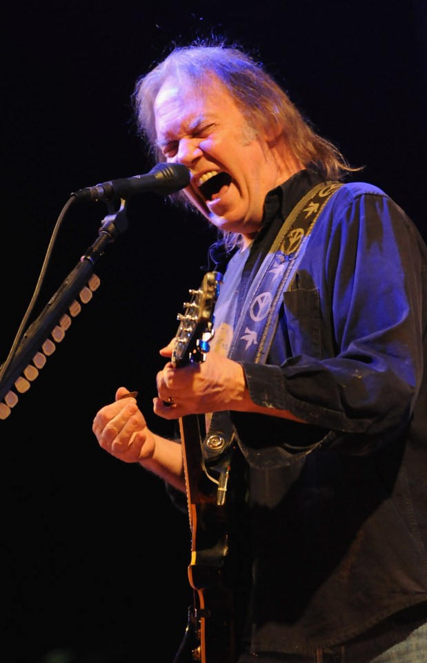 Neil Young performing on stage with a guitar.
