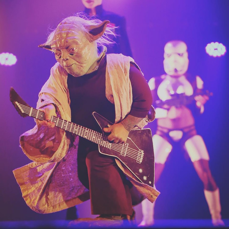Yoda playing guitar onstage during a burlesque performance of Star Wars.