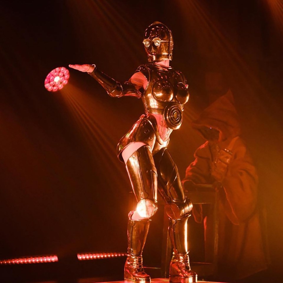 A burlesque dancer dressed as C-3PO performs on stage.