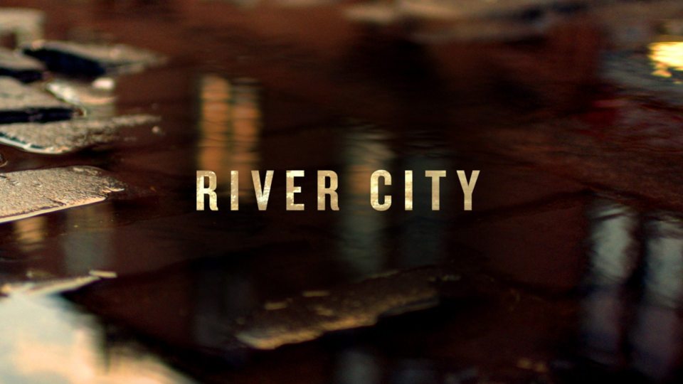 River City title card over a blurry image of a dark puddle reflecting city lights.
