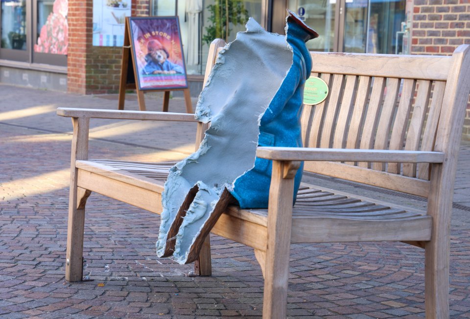 The remains of a vandalized Paddington Bear statue on a park bench.
