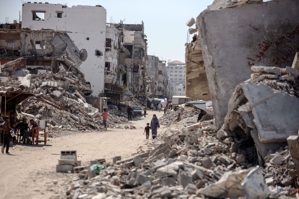 Palestinians walking amidst rubble and destroyed buildings in Khan Younis, Gaza.