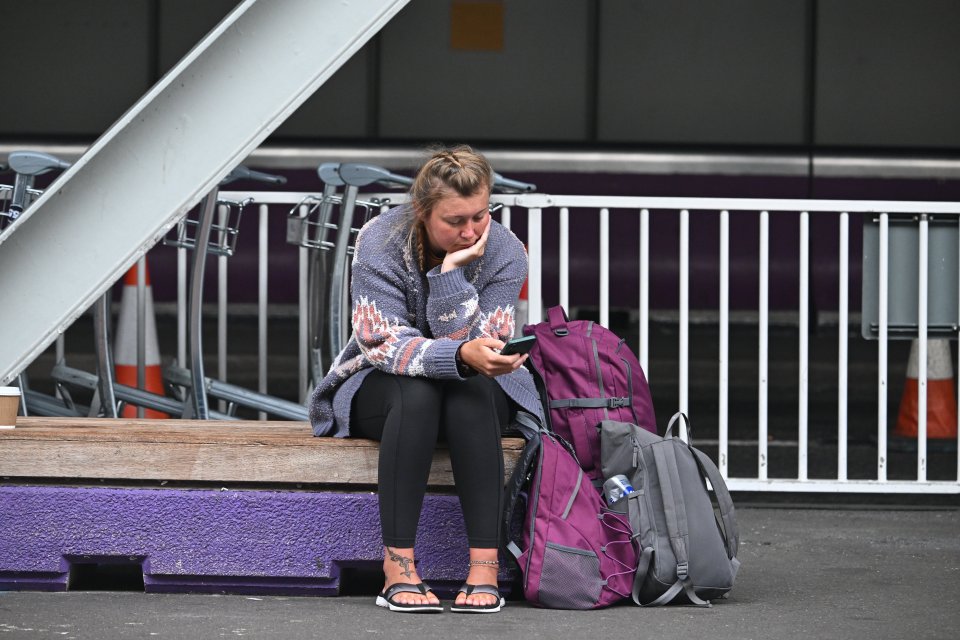 A passenger sits on a bench at Heathrow Airport Terminal 4, looking at her phone.