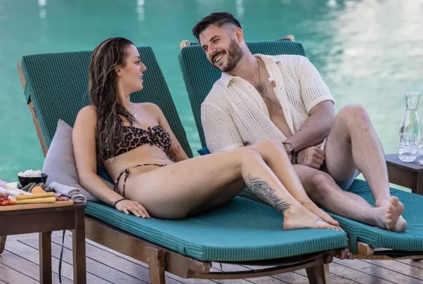 Couple relaxing on lounge chairs by a pool.