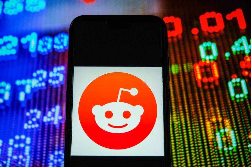 Photo illustration of the Reddit logo on a smartphone screen against a blurred stock market ticker.