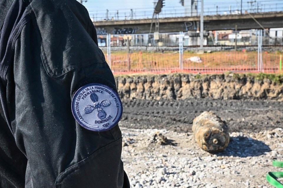 A bomb disposal expert's jacket with a patch, and a large unexploded WWII bomb in the background.