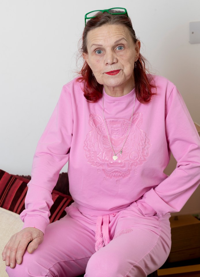 A woman in a pink tracksuit sits for a portrait.