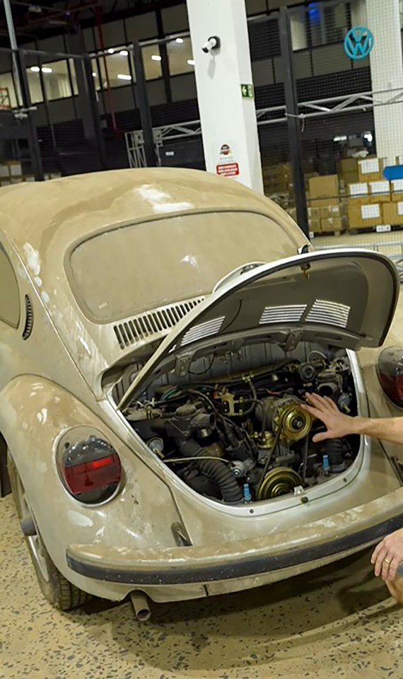 Dust-covered Volkswagen Beetle with its hood open, revealing its engine.
