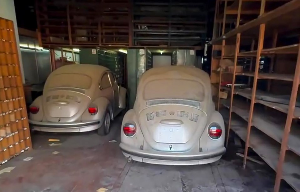Two dust-covered Volkswagen Beetles in a garage.
