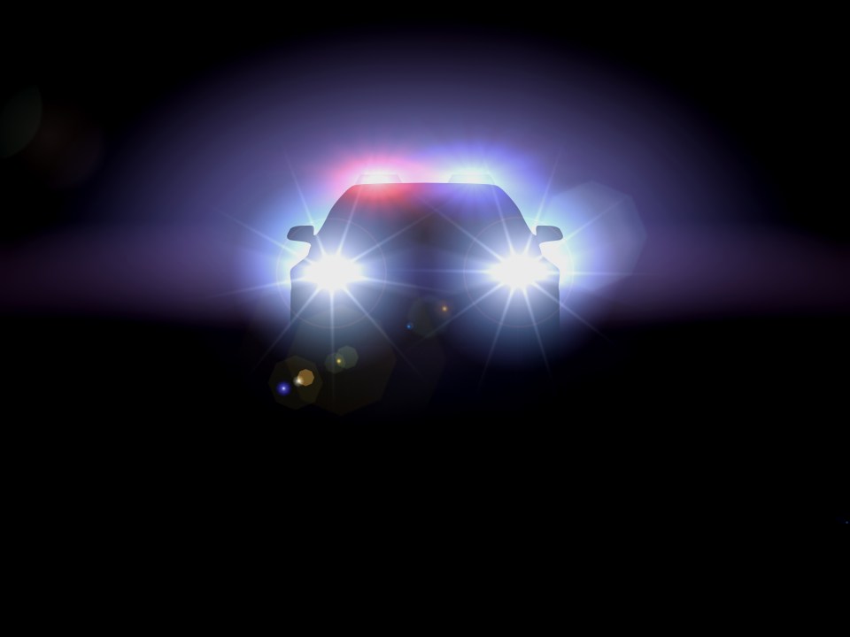 Silhouette of a police car at night with flashing lights.
