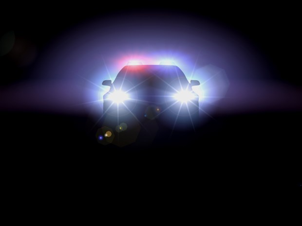 Silhouette of a police car at night with flashing lights.