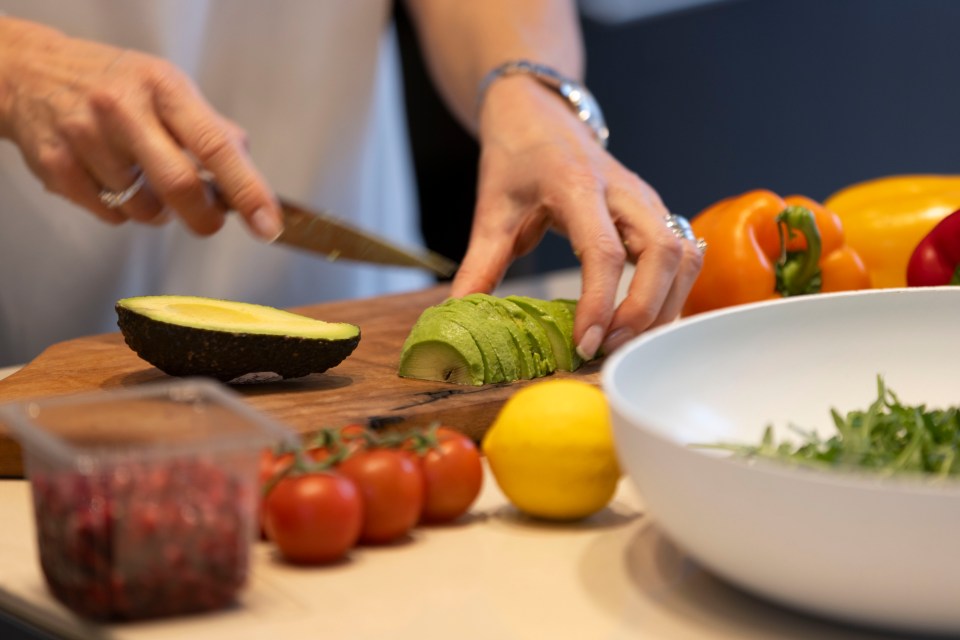 Woman slicing avocado on a wooden board.