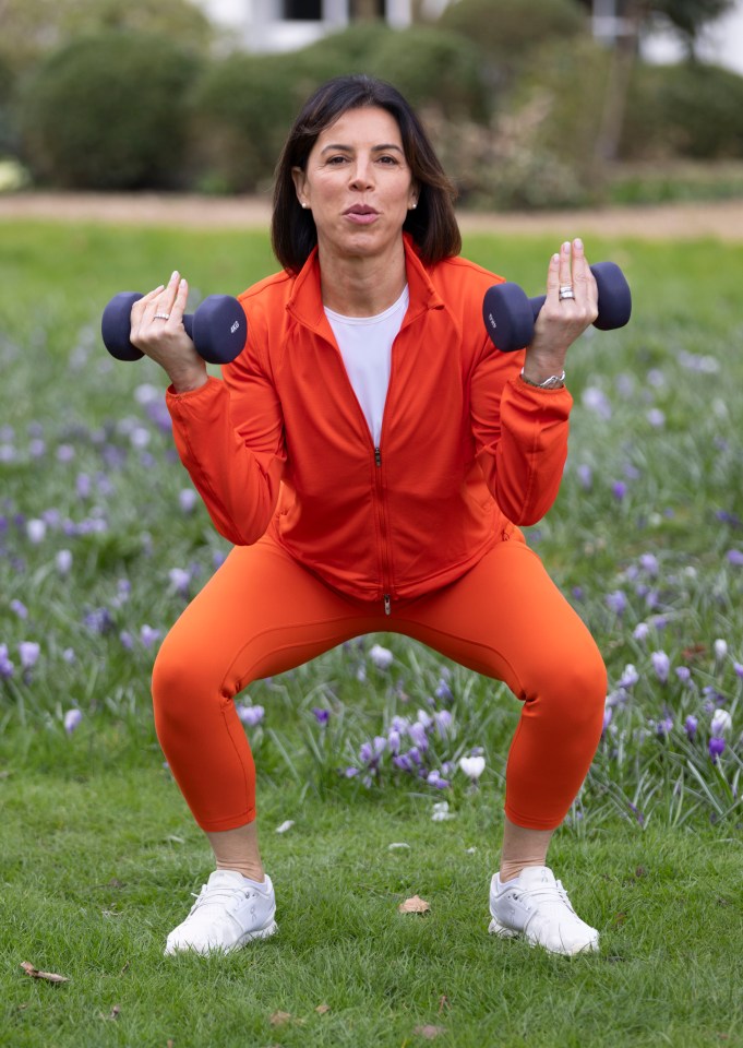 Woman in orange workout clothes squatting while lifting weights outdoors.