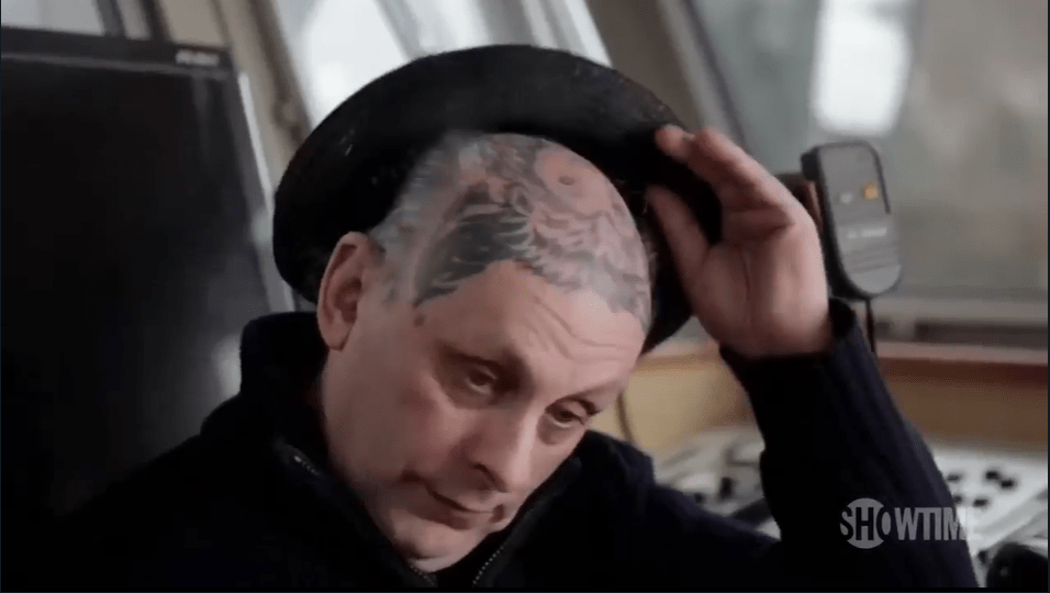 Man with a large head tattoo removing his hat.