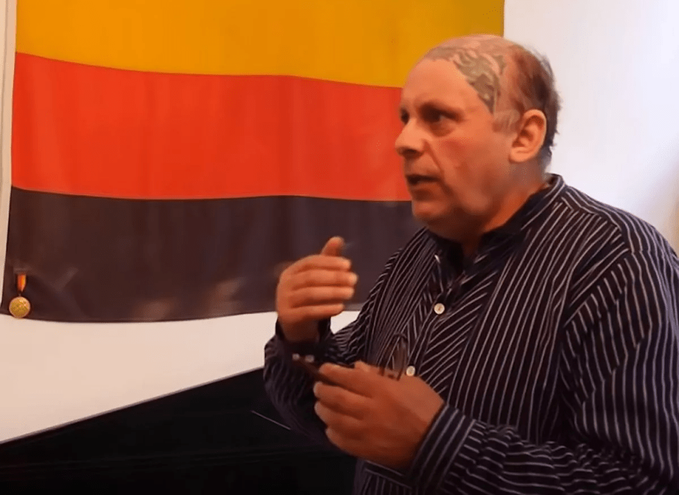 Man speaking in front of a flag.
